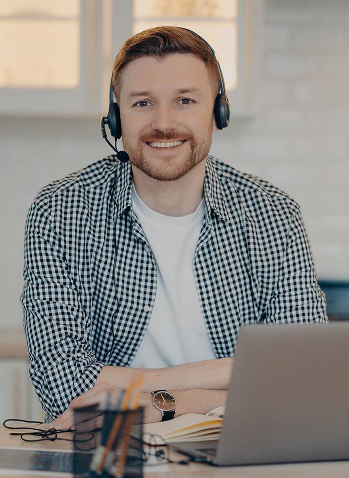 A friendly man sits in front of a notebook and wears a headset on his head. He uses Dynamics 365 Customer Service for customer support.